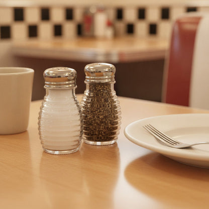 Close-up of ribbed beehive glass salt and pepper shakers with stainless steel tops on a classic diner table.