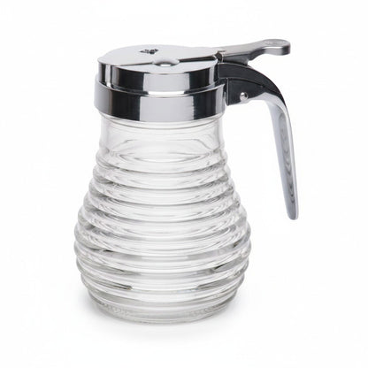 Clear glass Pancake House beehive syrup dispenser with ribbed sides, chrome lid, thumb lever, and curved handle on a white background.